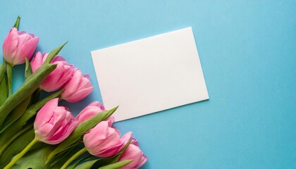 blank paper with pink flowers on a pastel blue background arranged flat and viewed from above with space for text