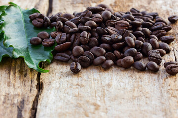 Coffee beans and fresh green leaf on wooden background