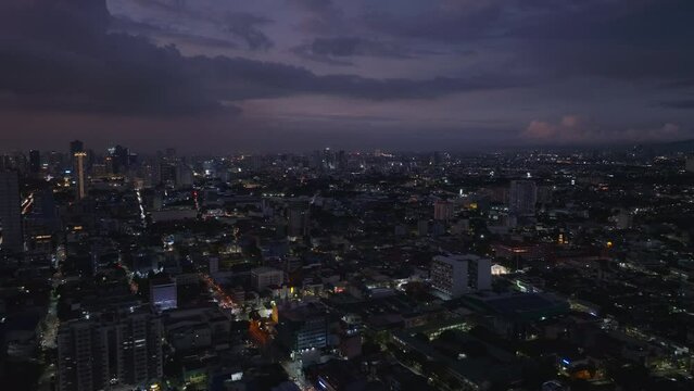 Aerial panoramic view of large city at dusk. Fly above metropolis at night. Clouds in dark sky. Manila, Philippines