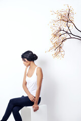 Girl, tree and branch with fashion in studio with thinking, peace and growth in nature by white background. Woman, person and model with leaves, memory and relax on chair for ecology, art or ideas