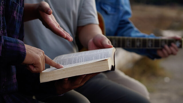 Three men read,pray and studied the bible at the park and prayed together. sharing the gospel with a friend. Holy Bible study reading together on Sunday.Studying the Word Of God With Friends.Education