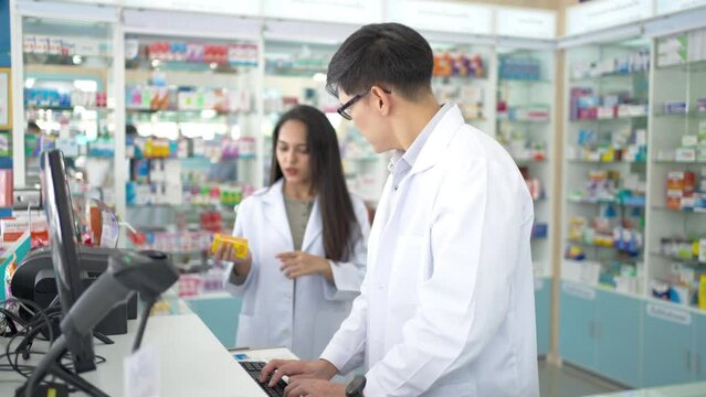 Medical pharmacy and health care business concept. Asian man and woman pharmacist colleague working together on computer checking medical product, drugs, medicine and supplements in modern drugstore.