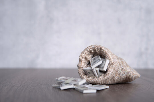 Closeup image of burlap sack overflowing with stacks of U.S. dollar bills with copy space. Prosperity, wealth, profit concept.