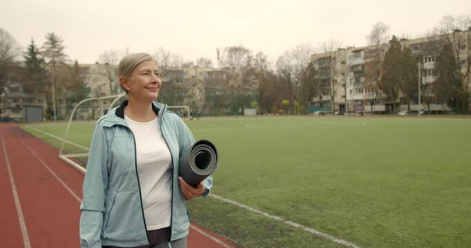 Senior woman carrying a fitness mat for training outdoors