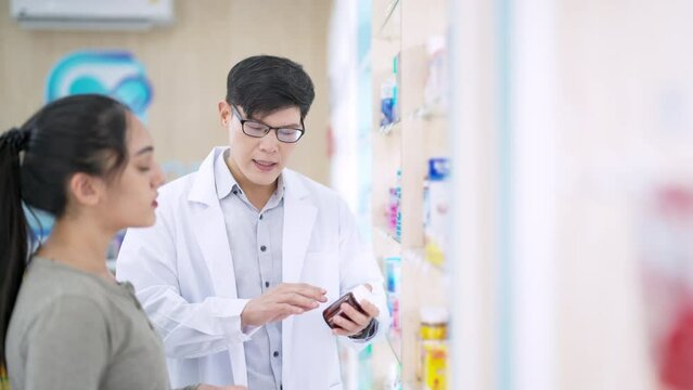 Medical pharmacy, hospital clinic healthcare providers concept. Asian man pharmacist medication recommendation medical product, drugs, medicine, and supplements to woman patient customer at drugstore.