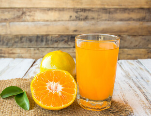 Glass of freshly pressed orange juice with sliced orange on wooden table