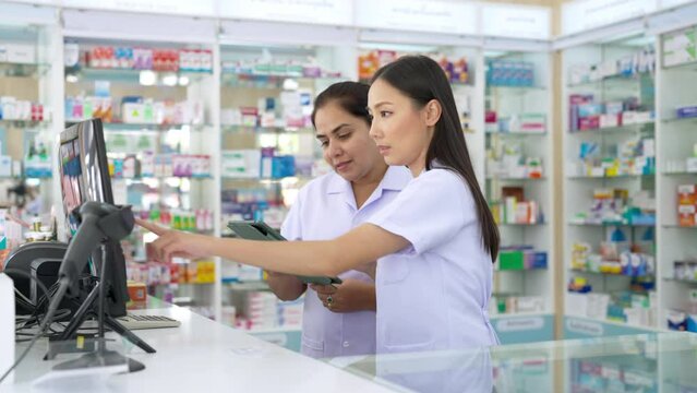 4K Medical pharmacy and health care business concept. Asian woman pharmacist colleague working together on computer checking medical product, drugs, medicine and supplements in modern drugstore.