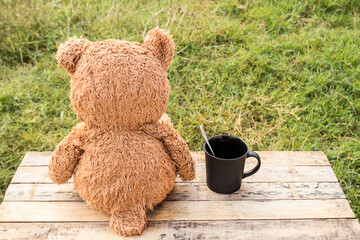 Teddy bear sitting backwards and coffee cup on a wooden table.