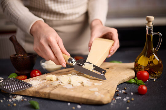 Woman slicing Piece of Traditional Italian Parmesan Hard cheese into flakes on a wooden cutting board at domestic kitchen