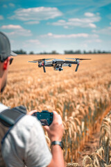 Man holding a remote controller while a drone hovers in the background over a wheat field