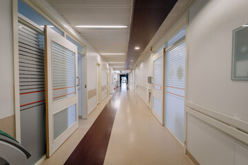 a hospital corridor with doors on either side. The hallway has a shiny floor, ceiling lights, and...