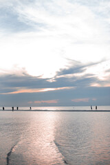 Obraz premium Silhouettes of people on a sandbar at sunset on a beach.