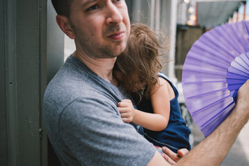 Man holds sleeping daughter while fanning her on hot summer day