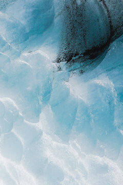 Textured wall of ice inside a glacier covered in black ash