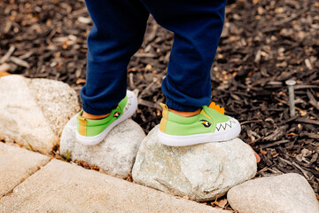 toddler balancing on rocks with green dinosaur shoes