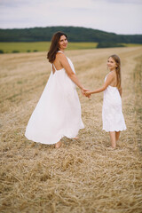 Fototapeta na wymiar Happy mother and daughter in summer dresses walking on the field