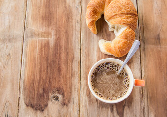 Croissant and coffee for breakfast on old wooden table