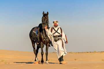 Arabian horseback archer walking with his arabian stallion through the desert dunes