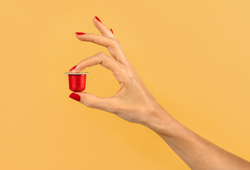 Female hand holding red coffee capsule in yellow studio