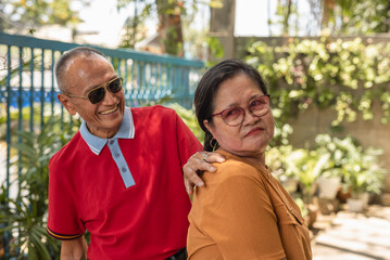 Elderly Asian couple in an outdoor setting, woman gently refusing husband's embrace