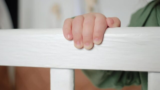 Close up of unknown baby infant boy stands in white kids bed and holding on to handrail. Childhood concept