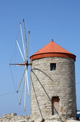 Fototapeta na wymiar Old Greek Windmill with Blue Sky Background by The Port in Rhodes, Greece