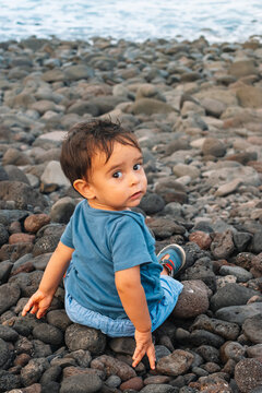 A young child is sitting on a pile of rocks, looking up at the camera. The image has a calm and peaceful mood, as the child seems to be enjoying the moment and taking in the surroundings