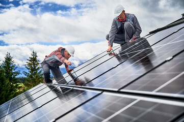 Electricians installing photovoltaic solar panels on roof of house. Men engineers in helmets...