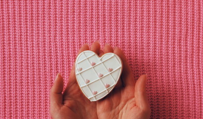 A Gentle Touch of Sweetness. Hand Presenting a Heart-Shaped Cookie on a Pink Knitted Texture