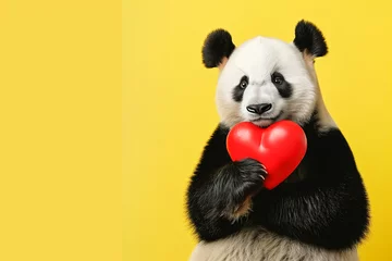 Wandaufkleber Cute smiling panda is holding a red heart as a gift for Women's Day, Mother's Day, Valentine's Day or wedding. Isolated on yellow background. Copy space for text © Patrik