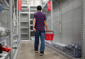 Man carrying a shopping basket, walking among the empty shelves. Stores closing down during the...