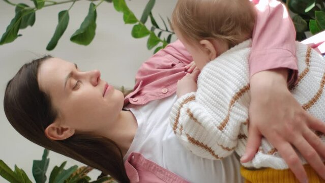 Vertical footage of happy caring young mom enjoying breastfeeding baby, motherhood, emotional bonding with cute little son. Hungry infant child touching mums face, drinking milk from mothers breast