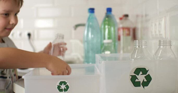 Child boy tries to help sort plastic for recycling in the kitchen at home. A boy child unscrews plastic caps from bottles and places them separately. Eco friend concept, children.
