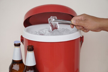 Close up hand hold tong to catch ice cube from red ice bucket cooler to prepare beverage. Concept, Mix drink for beer or alcohol beverage or cocktail with ice for more testy. 