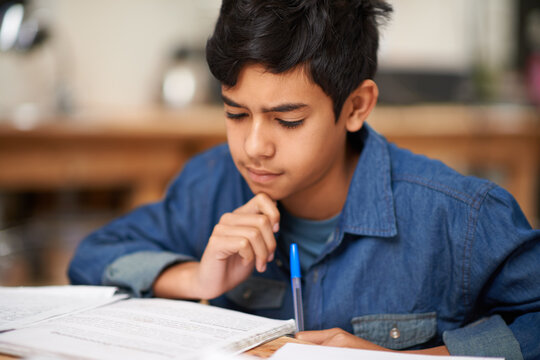 Student, boy and reading in home for study with thinking, problem solving and homework assessment by table. Child, education or knowledge with books in dining room for concentration on school project