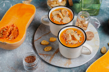 Roasted butternut squash soup with cream and pumpkin seeds on two white mugs.