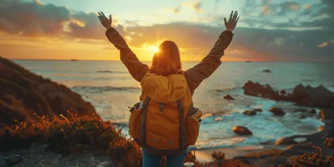 Foto auf Glas Confident woman with backpack with arms up relaxing at sunset seaside during a trip , traveler enjoying freedom in serene nature landscape, Generative AI © Focal Imaging