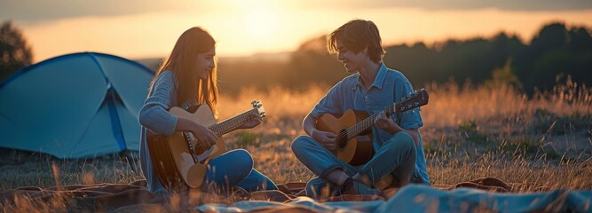 A teenage boy and girl play guitar next to the tent.