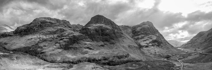 This super panorama unveils the Three Sisters majestic contours from a drone perspective, with the sweeping Glen Coe valley unfolding beneath a dramatic Scottish sky - obrazy, fototapety, plakaty