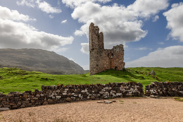 The historic remnants of Ardvreck Castle, amidst the green highlands and under a dynamic sky, offer a glimpse into Scotland's storied past