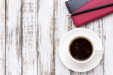 Coffee cup and notebook on white wooden table background