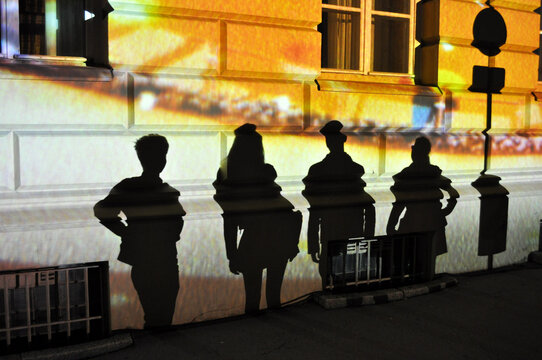 Schatten im Lichtspiel: Personen an einer farbig beleuchteten Hauswand