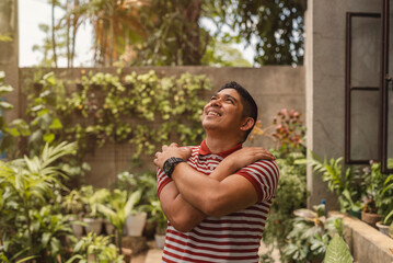 Middle aged Asian man embracing himself and looking upwards with an expression of peace