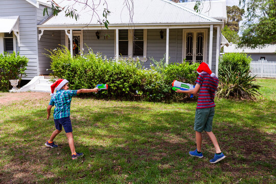 Brothers pointing blaster pistols in Christmastime water fight