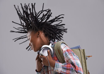 Black child, music and hair flip of a teenager with hip hop and rap audio in a studio. Excited, backpack and student with headphones for radio before school with a happy smile and grey background
