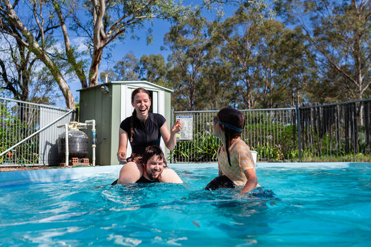 Teenagers and young adults playing shoulder wars in backyard swimming pool