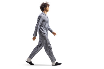 Full length profile shot of a young man in pajamas and slippers walking