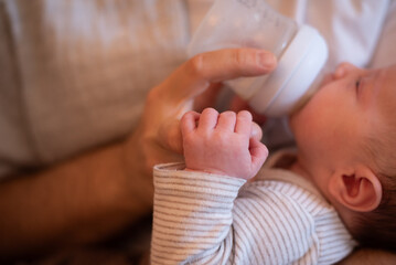 Hands of mom and newborn baby. child eat milk formula from bottle. Baby hold mom's finger. Copy space for text. Beagle clothes. No face. Love and hands care