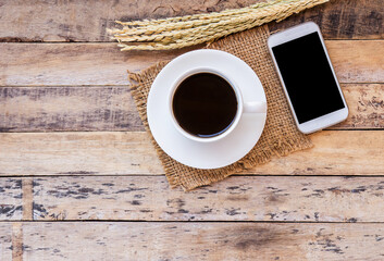 Ears of wheat and cup of coffee with smart phone on wooden table