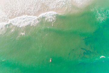 drone aerial overhead view of a surfer with a red surfboard in a beach of turquoise water
